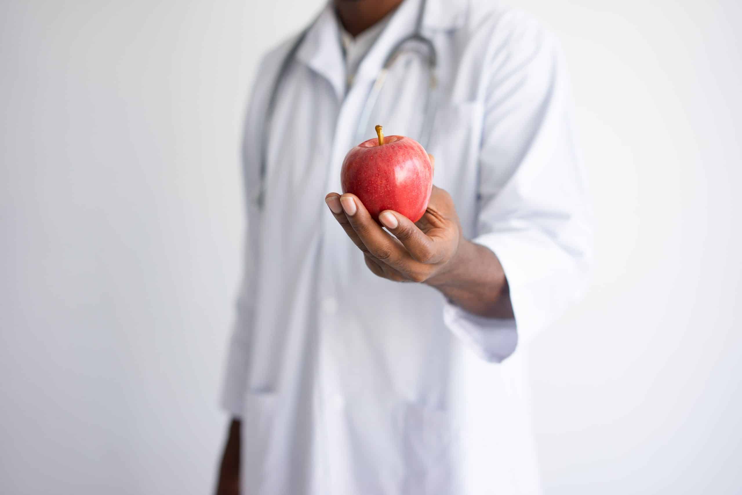 Closeup of black male doctor holding and offering red apple